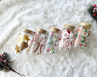 May include: Six glass jars with wooden lids decorated with Christmas themes. The jars feature designs of gingerbread men, candy canes, Christmas lights, and the words "Ho Ho Ho".