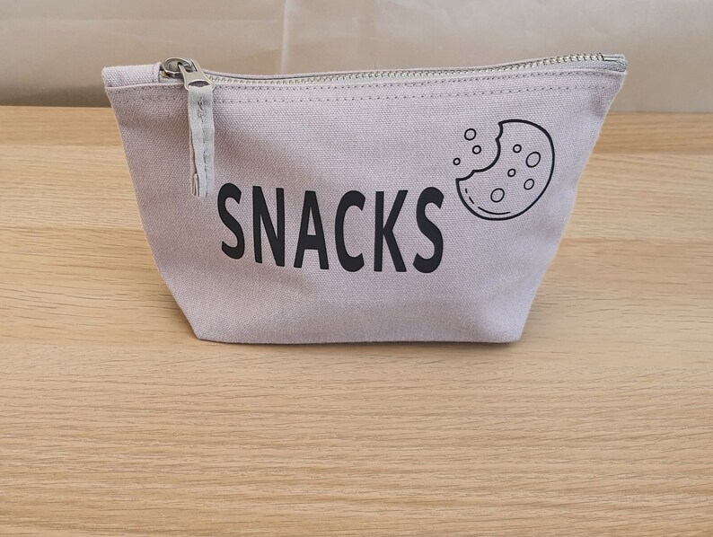 May include: A light grey canvas zippered pouch with a black cookie graphic and the word "SNACKS" printed on the front.