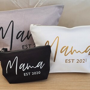 Puede incluir: Tres estuches con cremallera con la palabra "Mama" en diferentes fuentes y colores. Los estuches son grises, blancos y negros. El texto en el estuche gris es negro, el texto en el estuche blanco es dorado y el texto en el estuche negro es blanco. Cada estuche tiene el a&ntilde;o "EST 2020" o "EST 2021" impreso debajo de la palabra "Mama".