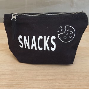 May include: Black canvas zippered pouch with the word "SNACKS" printed in white and a white outline of a cookie with a bite taken out of it.