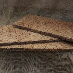 May include: Three brown cork tiles stacked on top of each other on a brown hessian background.