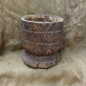 May include: A large, dark brown wooden mortar with intricate carvings around the top and bottom. The mortar is sitting on a hessian surface.