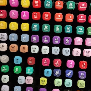 Könnte beinhalten: Nahaufnahme eines Rasters von farbigen Kunstmarkern. Jeder Marker hat eine farbige Kappe mit einer Nummer und dem Farbnamen aufgedruckt. Die Farben umfassen Rot, Rosa, Gelb, Grün, Blau und Lila.