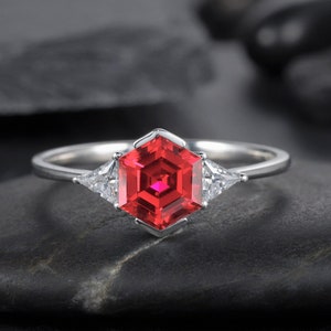 May include: A silver ring with a red hexagonal gemstone and two smaller triangular gemstones on either side.