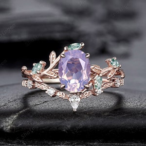 Könnte beinhalten: Ein zarter Ring aus Roségold mit einem großen ovalen Amethyst, der von kleineren grünen Edelsteinen und Diamanten umgeben ist. Der Ring hat ein Blattdesign.