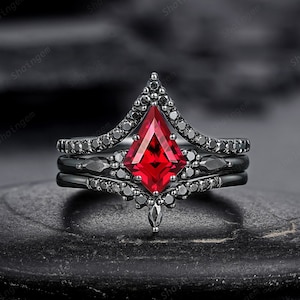 May include: A black and red three-piece ring set with a large, red, pointed gemstone in the center. The ring is set in a black metal band with small black gemstones.