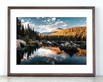 May include: A framed photograph of a mountain lake with a reflection of the sky and clouds in the water. The lake is surrounded by trees and mountains in the background.