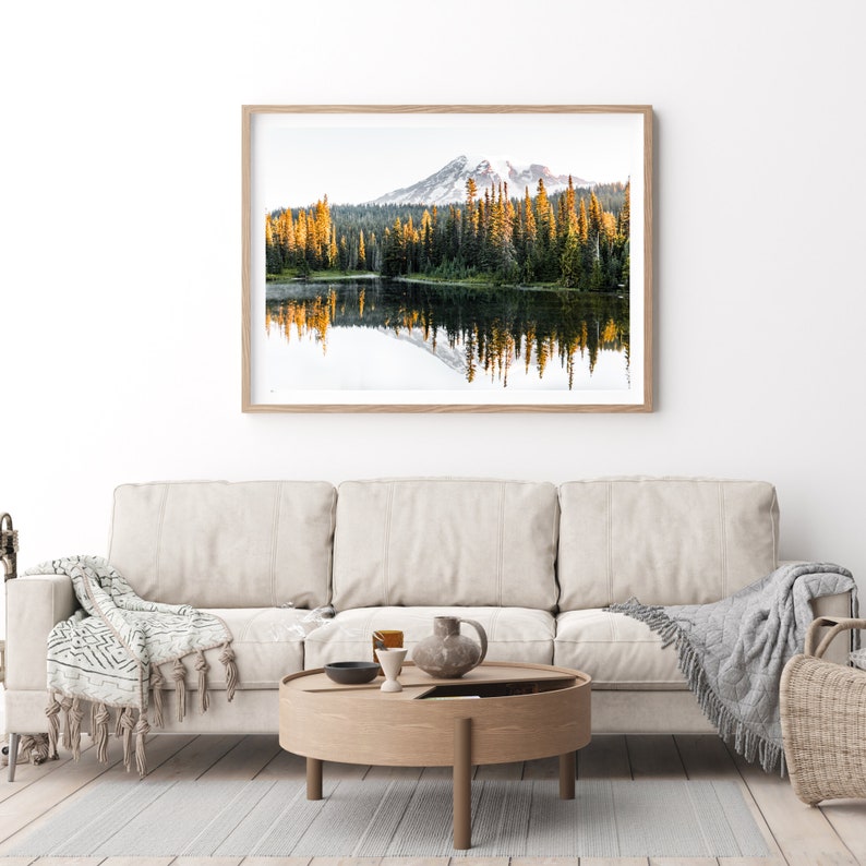 Mountain reflecting in lake with trees in mt rainier national park wall photo framed above couch in living room.