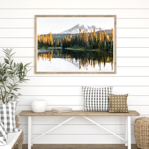 Mountain reflecting in lake with trees in mt rainier national park wall photo framed above bench in house.
