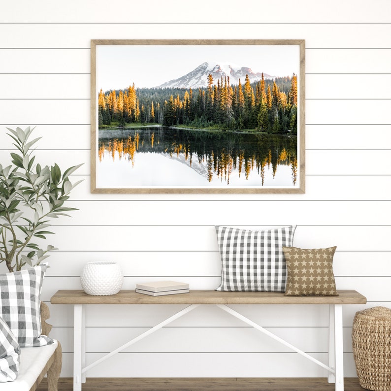 Mountain reflecting in lake with trees in mt rainier national park wall photo framed above bench in house.