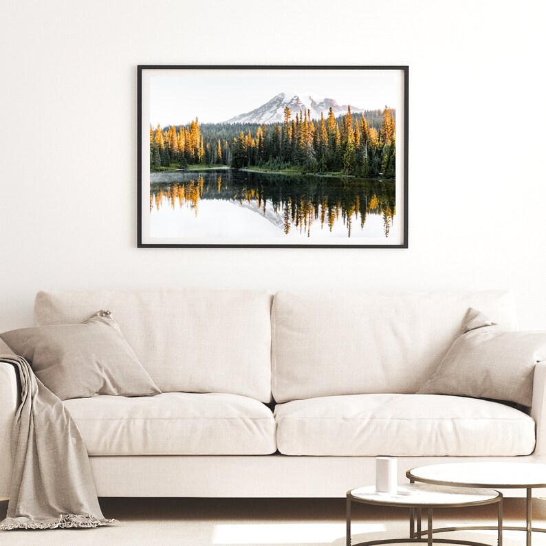 Mountain reflecting in lake with trees in mt rainier national park wall photo framed above couch in living room.
