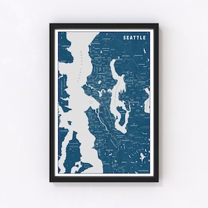 May include: Framed map print of Seattle in shades of blue and white. The map highlights the city's layout, including Puget Sound and Lake Washington. The word "SEATTLE" is printed at the top. The print is encased in a black frame.