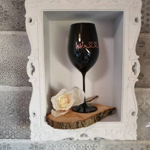 Może przedstawiać: Czarna kieliszek do wina z napisem "bestie" i sercem w kolorze różowym na boku, stojący na drewnianym plastrze w białej, ozdobnej ramie.