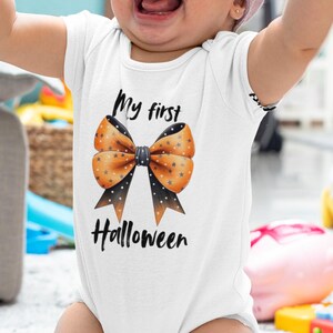 Könnte beinhalten: Ein weißer Baby-Body mit einer Halloween-Schleife mit der Aufschrift "My first Halloween". Die Schleife ist orange mit schwarzen Punkten und schwarzen Bändern. Das Baby trägt ein rosa Stirnband.
