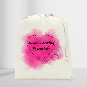 Könnte beinhalten: Eine weiße Kordeltasche mit einem rosafarbenen Aquarell-Herzdesign. Das Herz hat eine gestrichelte Linie darum und den Text "Susan's Sewing Essentials" im Inneren. Eine Nadel und ein Faden sind neben dem Herzen gezeichnet.