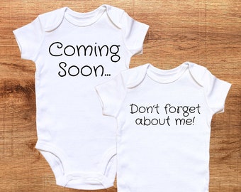 May include: Two white baby onesies with black text. The onesie on the left says "Coming Soon..." and the onesie on the right says "Don't forget about me!"
