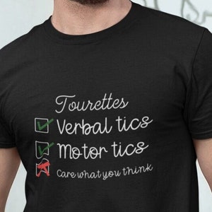 May include: A black t-shirt with white text that reads "Tourettes", "Verbal tics", "Motor tics", and "Care what you think". The text is in a checklist format with checkmarks next to the first two lines and a red X next to the last line.
