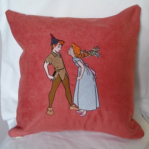 May include: A red cushion with an embroidered image of Peter Pan and Wendy from the Disney film Peter Pan. Peter is wearing a green outfit and Wendy is wearing a blue dress.