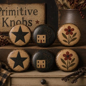 Könnte beinhalten: Sechs dekorative Türknöpfe aus Holz mit rustikaler, Vintage-Ästhetik. Designs umfassen einen schwarzen Stern, ein Haus und eine rote Blume. Die Knöpfe werden auf einer Holzoberfläche mit einem Schild mit der Aufschrift "Primitive Knobs" ausgestellt.
