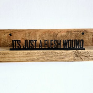 May include: A wooden shelf with a black metal sign that reads "It's just a flesh wound".