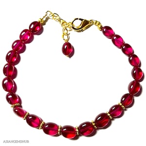 Op de afbeelding: Een rode edelsteen armband met gouden accenten. De armband is gemaakt van ovale kralen en heeft een karabijn sluiting.