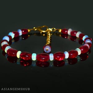 Puede incluir: Un brazalete hecho de cuentas ovaladas rojas y blancas alternas. El brazalete tiene un cierre dorado.