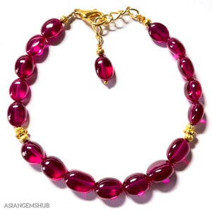 May include: A pink gemstone bracelet with gold accents. The bracelet is made of oval-shaped gemstones and has a gold clasp.