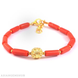 May include: A red coral bracelet with a gold bead in the center. The bracelet is made of small, rectangular coral beads and has a gold clasp.
