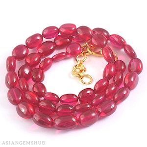 Pode incluir: Um fio de contas de rubi vermelho escuro, de forma oval, enfiadas em uma corrente de ouro com um fecho.