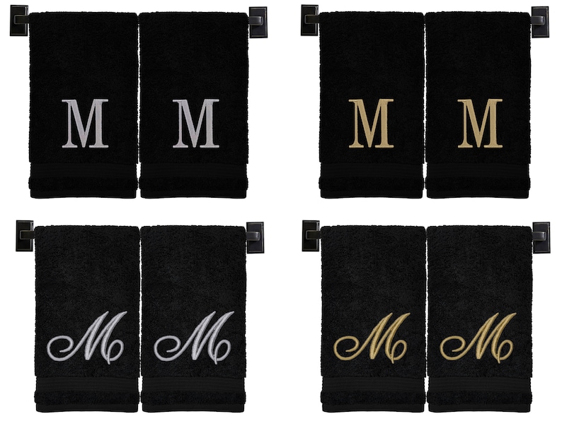 May include: Two sets of black hand towels with embroidered letter "M" in different styles. The first set has silver "M"s, the second set has gold "M"s, the third set has silver cursive "M"s, and the fourth set has gold cursive "M"s.