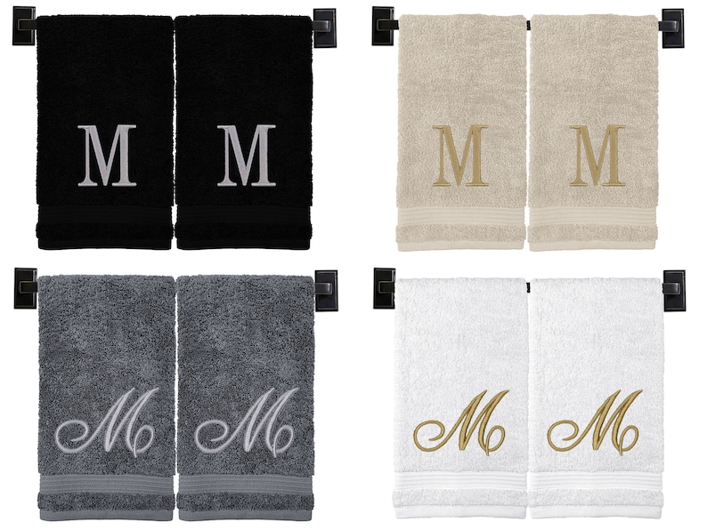 May include: Set of two hand towels in four different color combinations: black with silver embroidery, gray with silver embroidery, beige with gold embroidery, and white with gold embroidery. Each towel features a single letter "M" embroidered in the center.