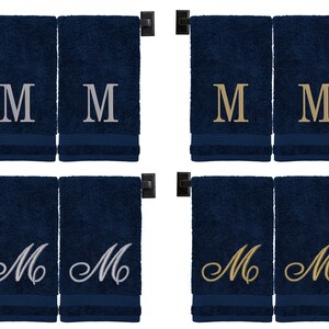 May include: Four navy blue hand towels with embroidered letter "M" in different styles. Two towels have silver "M", one has gold "M", and one has a cursive silver "M".