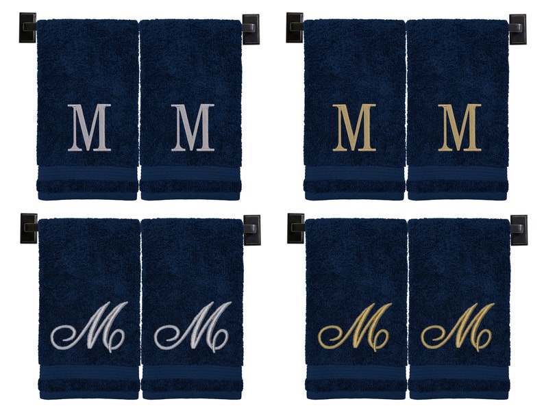 May include: Four navy blue hand towels with embroidered letter "M" in different styles. Two towels have silver "M", one has gold "M", and one has a cursive silver "M".