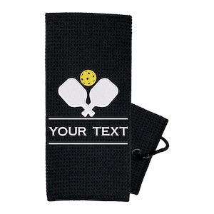 Pode incluir: Toalha de tecido waffle preto com um design branco de raquete e bola de pickleball. A toalha tem um la&ccedil;o para pendurar e diz "YOUR TEXT" em branco.