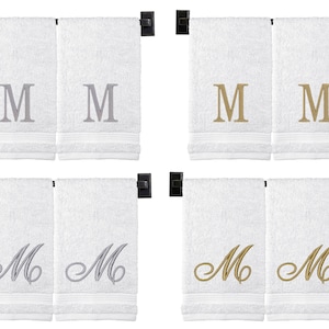 May include: Set of four white hand towels with embroidered letter "M" in silver and gold. Two towels feature a simple "M" and two towels feature a cursive "M".