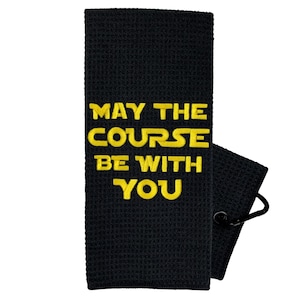 May include: Black golf towel with a yellow embroidered saying "May the course be with you."