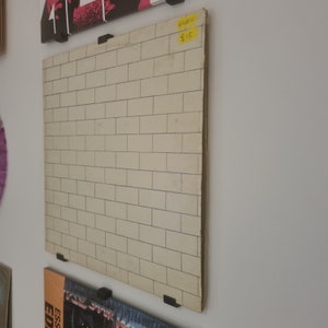 May include: A white vinyl record album with a brick wall design on the cover. The album is hanging on a wall with a yellow price tag that says "6.25".