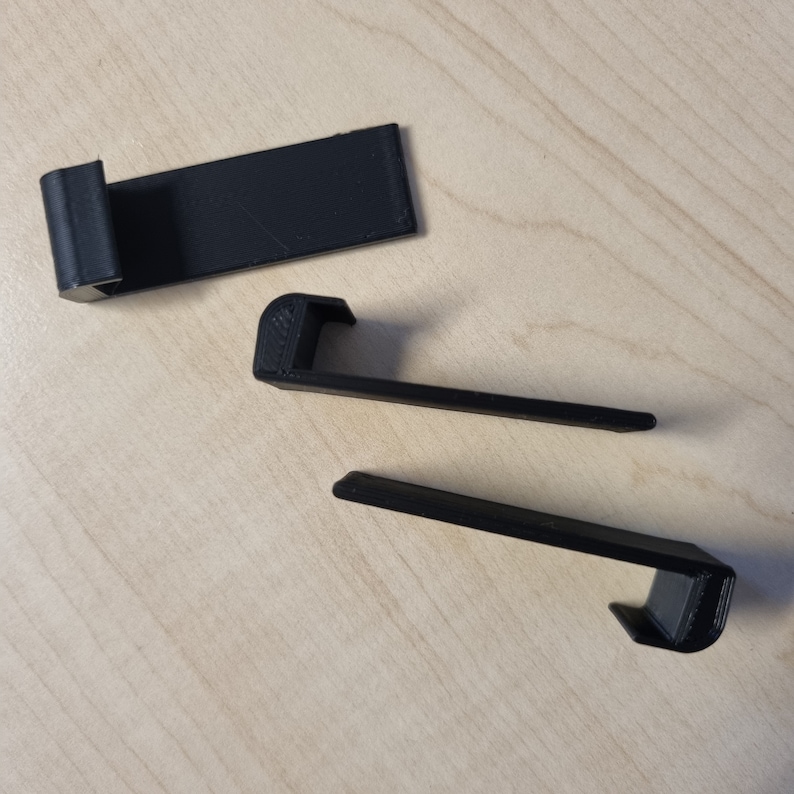 May include: Three black plastic hooks, two are curved and one is straight. The hooks are on a light brown wooden surface.