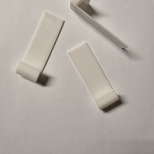 May include: Three white plastic hooks for hanging items. The hooks are designed to be attached to a wall or other surface.