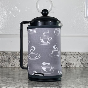 May include: A gray french press coffee maker with a white coffee cup design on the sleeve. The sleeve has the text "JAVA Skins" on it.