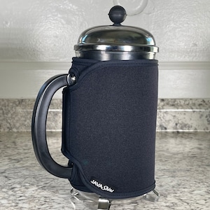 Pode incluir: Uma capa de neopreno preta para uma cafeteira de prensa francesa. A capa tem o texto "JAVA Street" impresso nela.