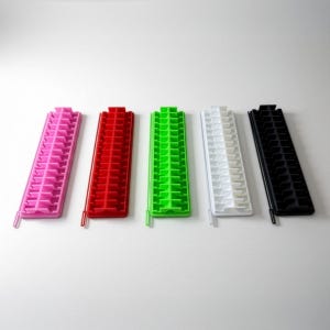 May include: Five colorful ice cube trays in pink, red, green, white, and black. Each tray has a rectangular shape with multiple small, individual ice cube molds. The trays are made of plastic and are arranged on a white surface.