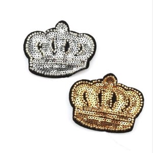 Może przedstawiać: Dwa naszywki do prasowania w kształcie korony. Jedna korona jest srebrna, a druga złota. Obie korony są pokryte cekinami.
