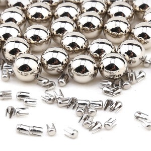 May include: A collection of silver metal round buttons with a shiny finish. The buttons have a pronged back for attaching to fabric.