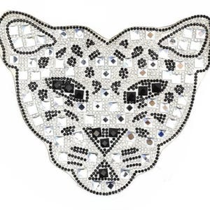 Può includere: Toppa decorativa a forma di testa di leopardo. È ricoperta di strass scintillanti e dettagli neri. Il design è intricato, con gli strass che formano il corpo principale e pietre nere che definiscono i tratti. Ideale per abbigliamento.