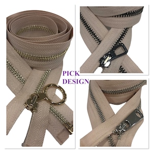 Puede incluir: Dos tiradores de cremallera con diferentes estilos. Un tirador de cremallera es dorado con un anillo, el otro es negro con un tirador rectangular. Ambas cremalleras son beige con un patrón de espiga.