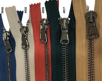 May include: Six different coloured metal zippers with silver pulls. The zippers are arranged from left to right in the following colours: blue, white, red, green, beige, and brown.