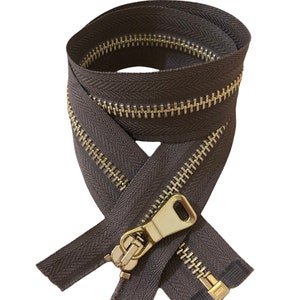 Puede incluir: Una cremallera marrón con un deslizador y una lengüeta de metal dorado. La cremallera está cerrada y los dientes son visibles.