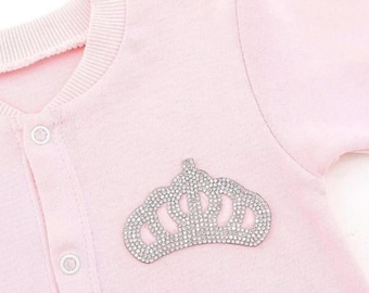 May include: A pink baby onesie with a sparkly silver crown design.