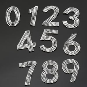 Puede incluir: Diez parches de hierro con forma de números del 0 al 9, cubiertos de diamantes de imitación plateados.